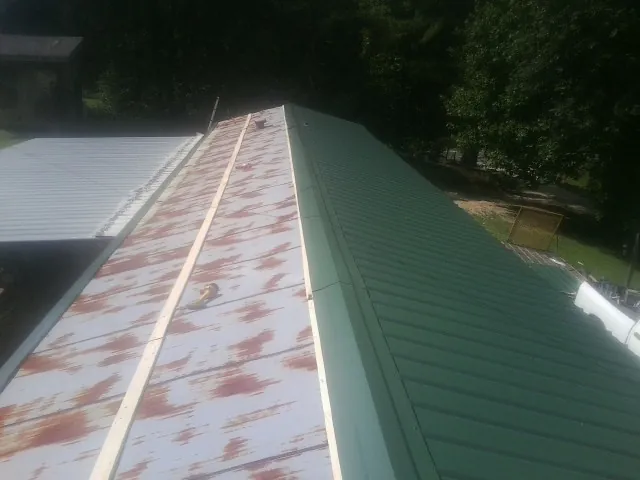 Old rusted panels beside newly installed green metal roofing — Wind Damage Roof Repair by Roofing Brothers in Saint Joseph