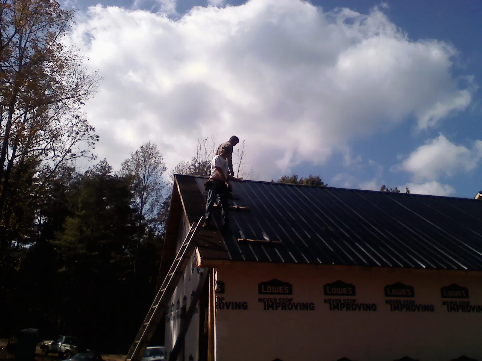Roofer fastening dark metal panels high against a cloudy sky, from a Roof Inspection job in Saint Joseph