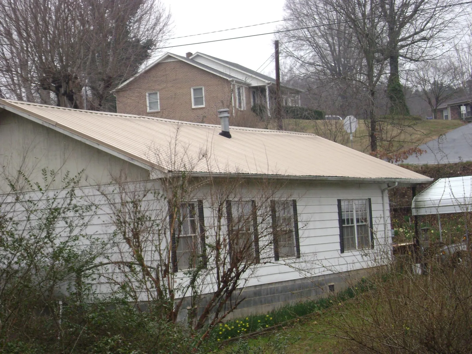 Tan metal roof on a white sided house set into a hillside — Commercial Roofing by Roofing Brothers in Saint Joseph